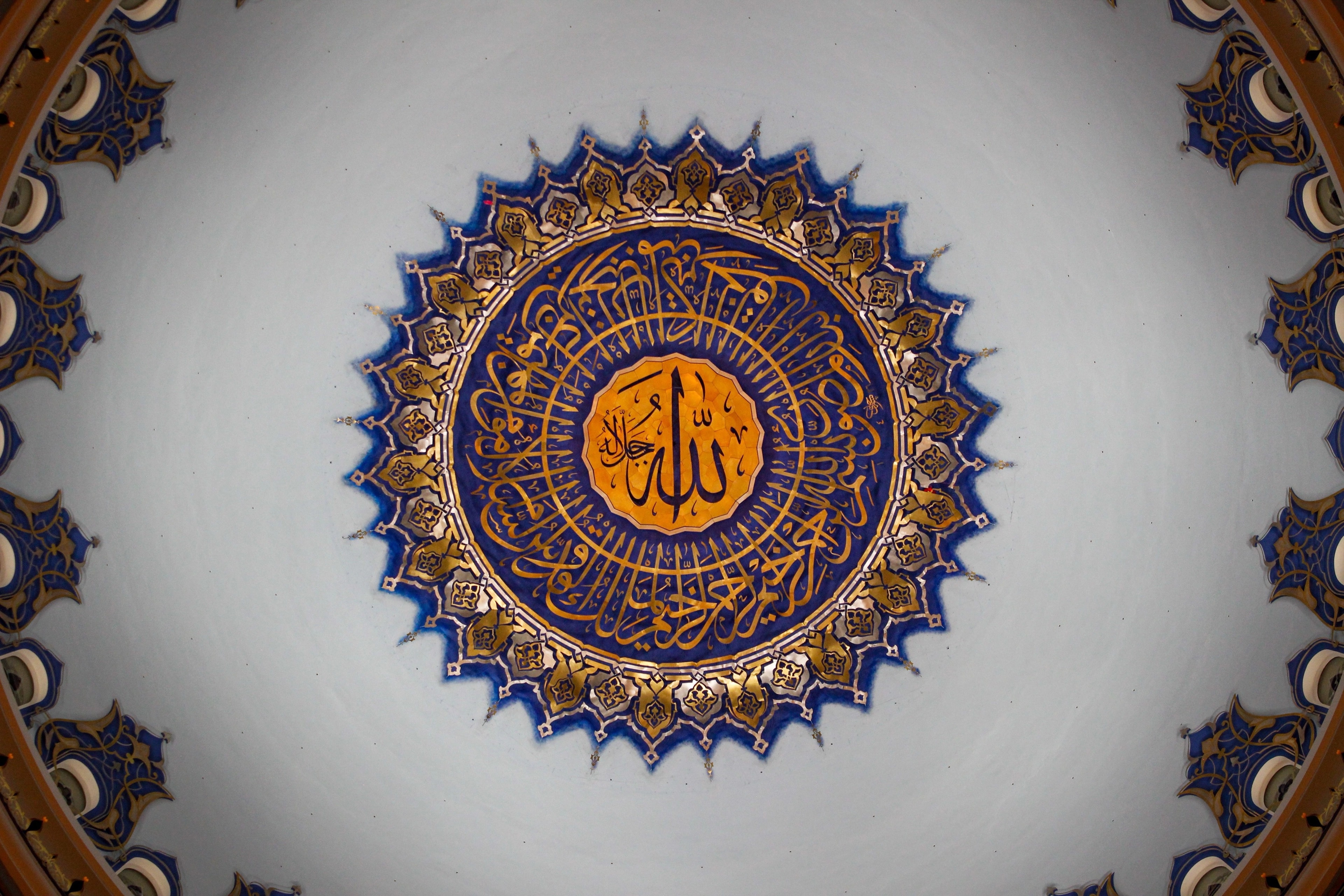 A mosque dome seen from below, with the name Allah at the center of a blue and gold medallion