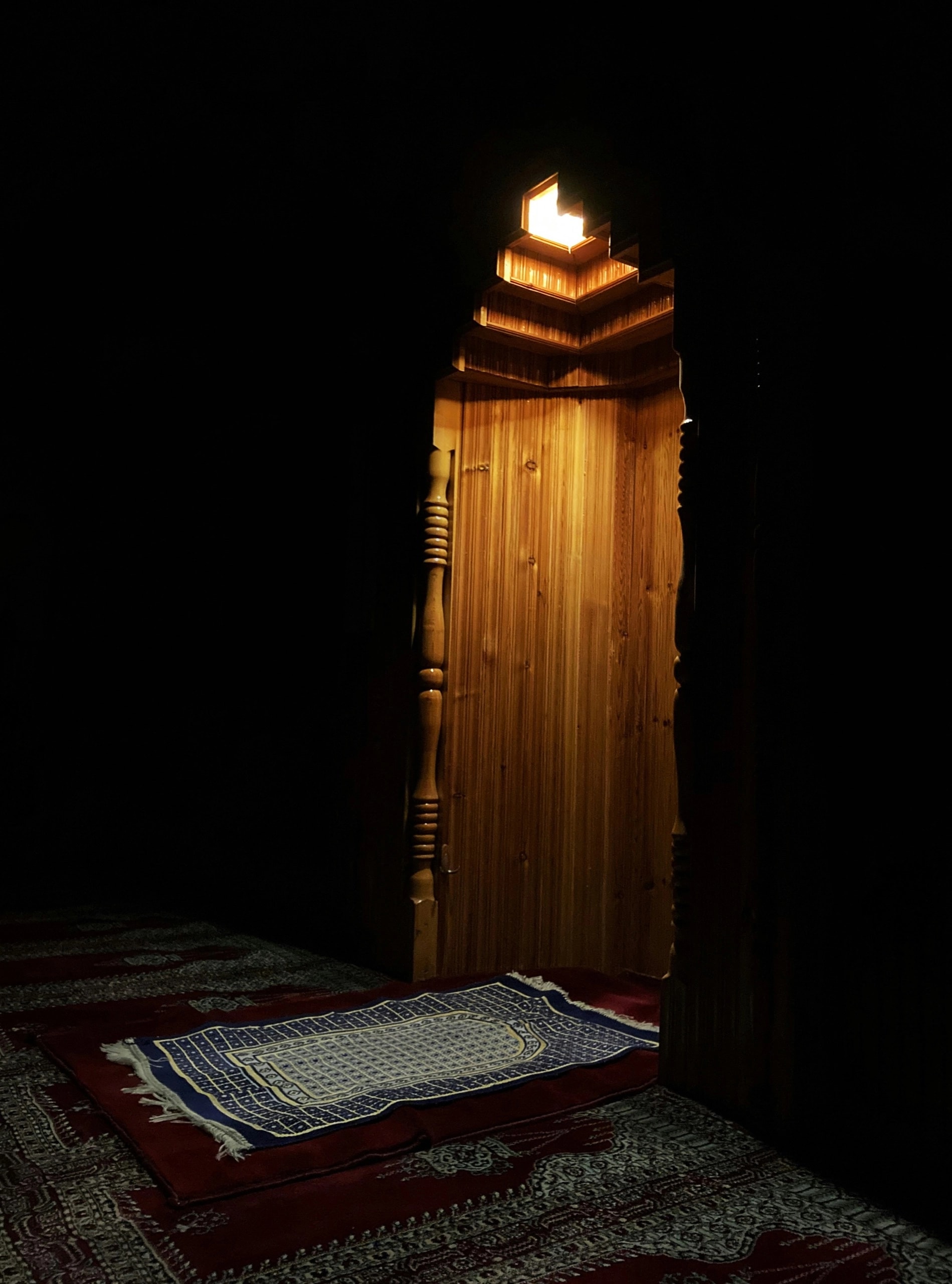 Soft light falling across a prayer mat before a mosque mihrab