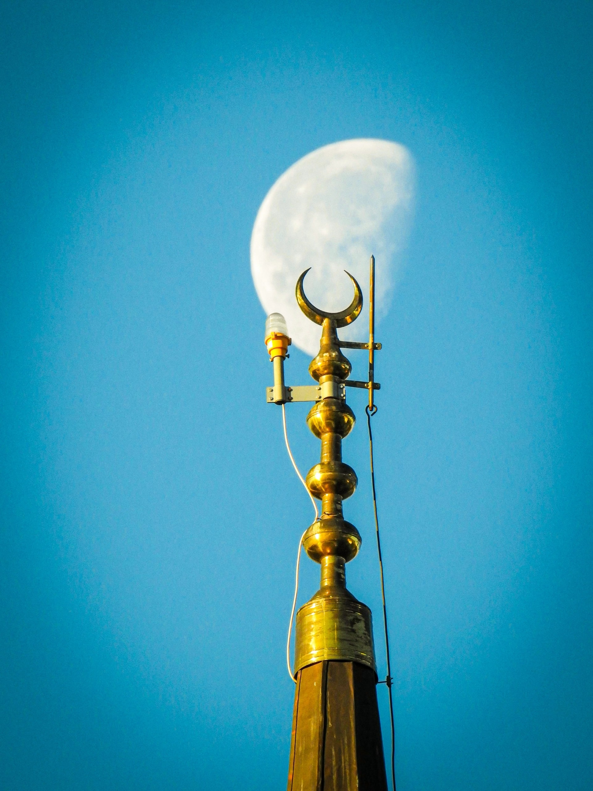 A gold crescent finial against the daytime moon