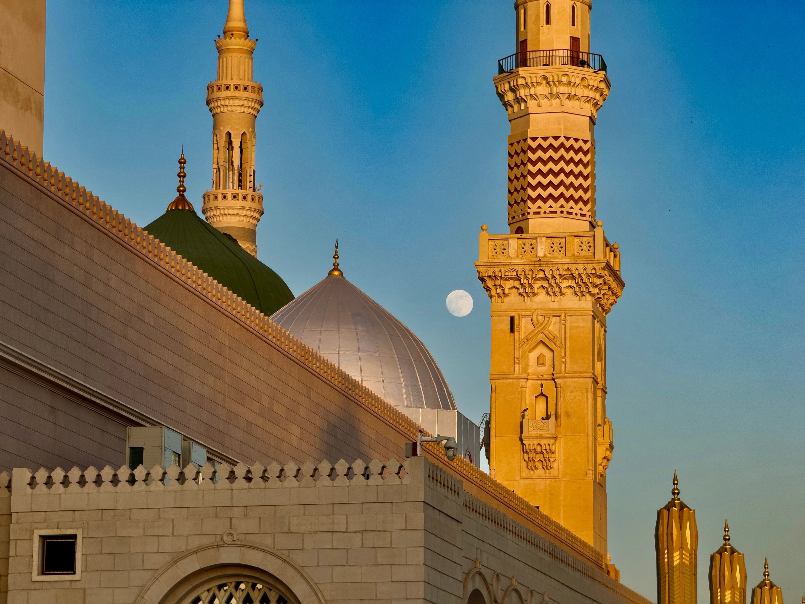 A minaret and domes in Medina at golden hour, with the moon above