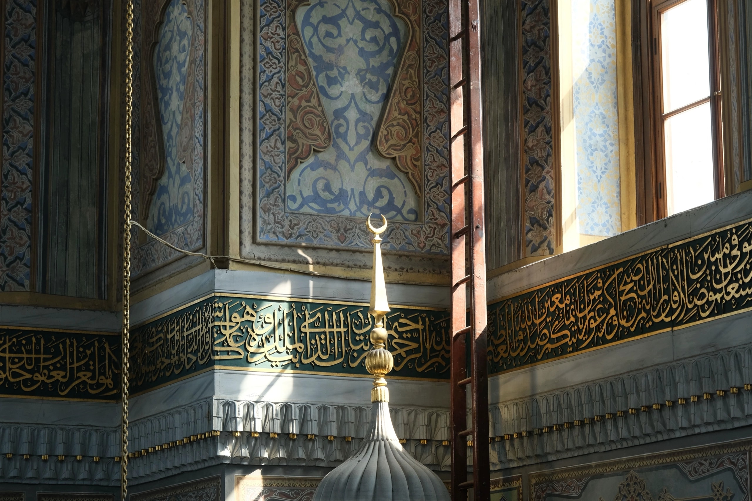 A band of gold Arabic calligraphy and a crescent finial inside a mosque